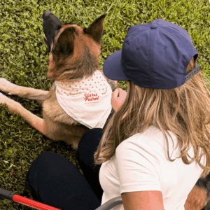 Yard Patrol tech sitting beside a large German shepherd wearing a branded bandana in a green yard