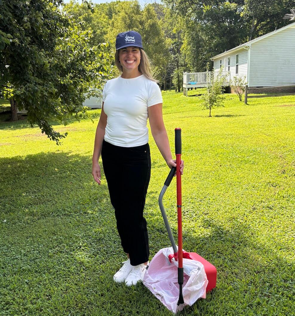Person standing in a neatly maintained yard with cleanup tools, representing Yard Patrol lawn care services.
