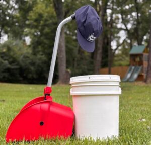 Professional pet waste removal tools, including a red scooper and white bucket, ready for residential dog poop cleanup in a grassy backyard in Middle Tennessee.